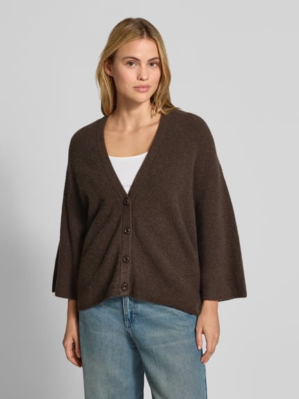 Frauenmodel trägt Oversized Cardigan aus Baumwoll-Anteil Modell 'DAMSVILLE' von American Vintage in Braun mit Strick-Optik und Knopfleiste, elastischer Material-Mix, V-Ausschnitt, Ganzkörperansicht von vorne.