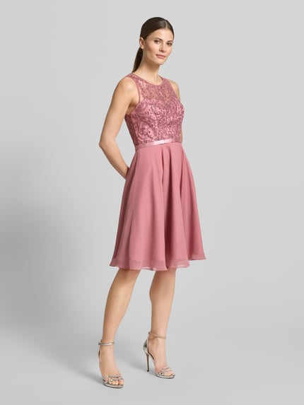 Frauenmodel trägt Cocktailkleid mit Rundhalsausschnitt von Luxuar in Altrosa, taillierter Schnitt, matt glänzender Stoff, Ganzkörperansicht von vorne.