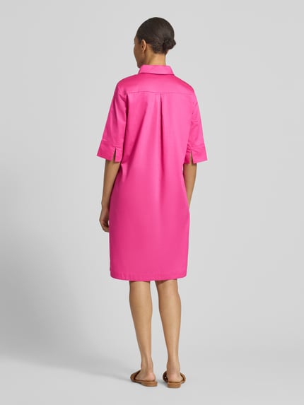 Frauenmodel trägt knielanges Hemdblusenkleid mit Eingrifftaschen von Christian Berg Woman aus pinker Baumwolle, gerade geschnitten, Rückansicht Ganzkörperansicht.