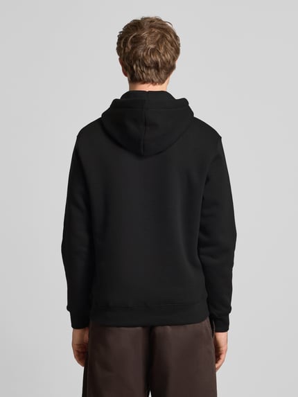 Männermodel trägt Relaxed Fit Hoodie aus Baumwoll-Mix mit Label-Detail von Alpha Industries, schwarzer Stoff, glatte Textur, Ganzkörperansicht Rückansicht. Baumwoll-Mix, Relaxed Fit, Känguru-Tasche, Kapuze mit Tunnelzug, Rückenlänge 68 cm, Ärmellänge 74 cm.