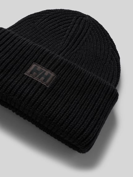 Produktfoto, Beanie in Strick-Optik mit Logo-Patch von Helly Hansen in Schwarz, grobes Strukturmuster, fixierter Bund, neutraler Hintergrund