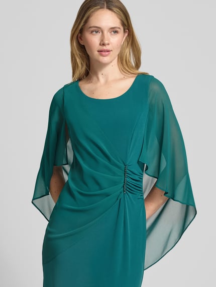 Frauenmodel trägt knielanges Cocktailkleid mit Rundhalsausschnitt von Vera Mont in Türkis, Elastischer-Material-Mix, Fledermausärmel aus Chiffon, Wickel-Optik, Zier-Applikation mit Strasssteinbesatz, knielang, rückenlanger Nahtreißverschluss, körpernahe Passform, Nahaufnahme Oberkörper.