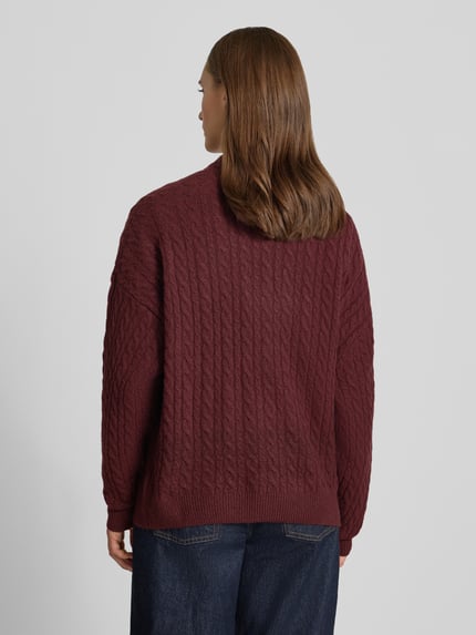 Frauenmodel trägt Oversized Fit Strickpullover mit Zopfmuster von REVIEW, bordeauxfarben, elastischer Material-Mix, Rückansicht, Ganzkörperansicht von hinten.