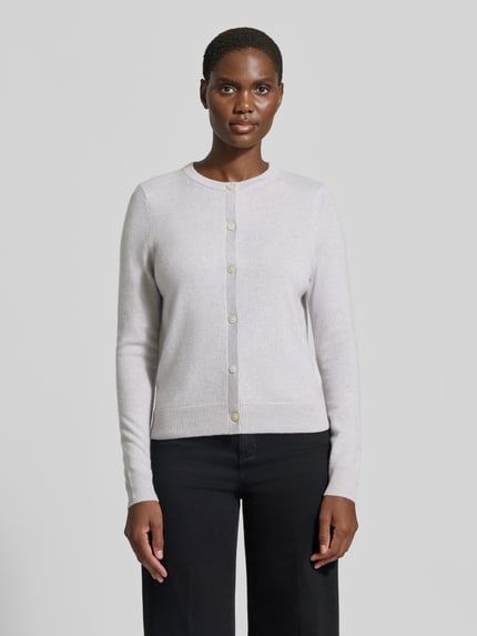 Frauenmodel trägt Strickjacke aus reinem Kaschmir mit durchgängiger Knopfleiste von Christian Berg Woman, hellgrau, gerippte Abschlüsse, Ganzkörperansicht von vorne.