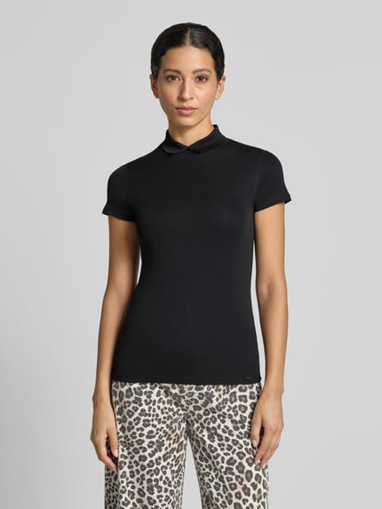 Kobiece modelka nosi Slim Fit T-Shirt mit hochschließendem Polokragen von Marc Cain, Mieszanka bawełny i elastanu, krój slim fit, Rękaw o dł. 1/2, Długość tyłu w rozmiarze 36: 59 cm, kolor czarny, gładka faktura, Ganzkörperansicht von vorne.
