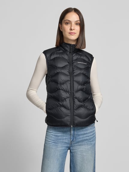 Frauenmodel trägt Steppweste mit Daunen-Federn-Füllung Modell 'HELIUM' von Peak Performance in Schwarz, Struktur mit Steppnähten, Ganzkörperansicht von vorne. Rückenlänge 62 cm, Schulterbreite 41 cm, Brustweite 49 cm, Slim Fit, Stehkragen, Reißverschluss, Label-Stitching.