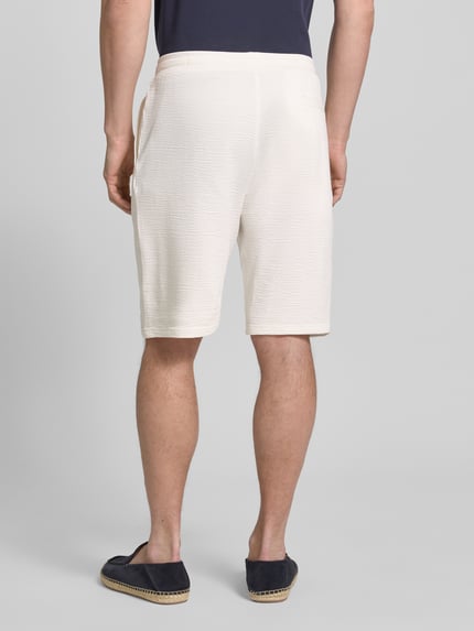 Männermodel trägt Relaxed Fit Bermudas aus Baumwoll-Mix Modell 'DETROIT' von s.Oliver RED LABEL in Creme, unifarben, Waffelstruktur, Ganzkörperansicht Rückansicht.