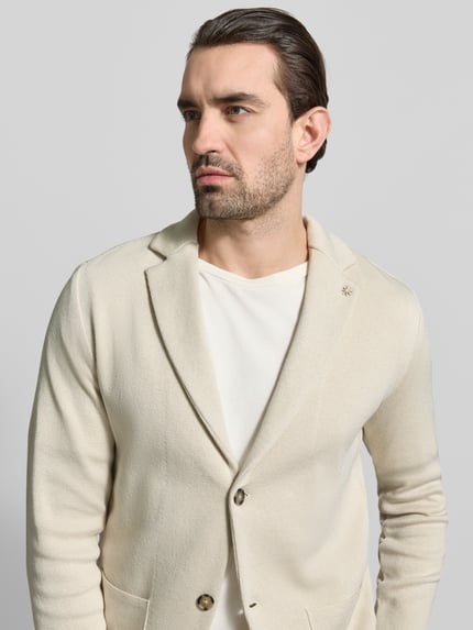 Männermodel trägt Slim Fit 2-Knopf-Sakko mit Reverskragen von Manuel Ritz aus reiner Baumwolle in Beige, Nahaufnahme Oberkörper.