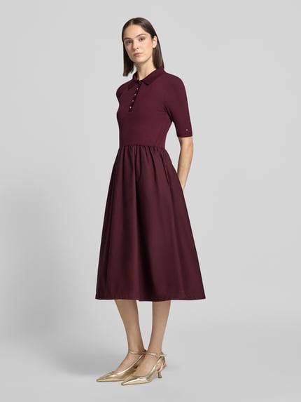 Frauenmodel trägt Midikleid mit Polokragen von Tommy Hilfiger in dunklem Bordeauxrot, glatte Textur, Ganzkörperansicht von vorne.
