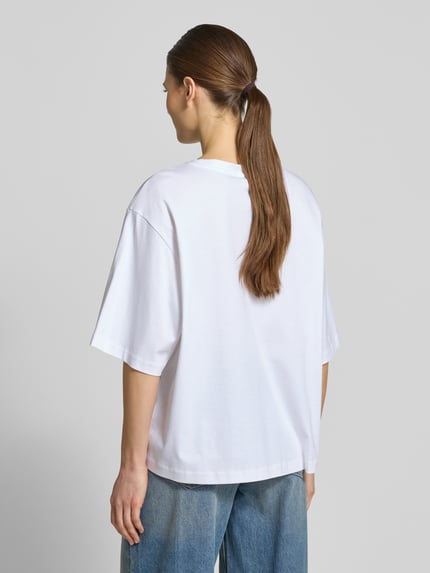 Frauenmodel trägt weißes Oversized T-Shirt mit Rundhalsausschnitt Modell 'PINARA' von Drykorn aus Baumwolle, Ganzkörperansicht Rückansicht.