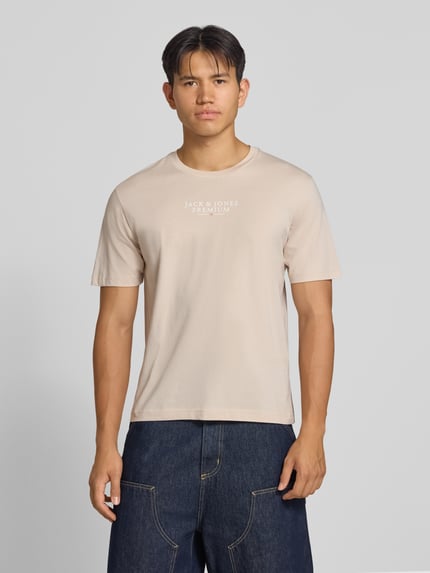Męski model nosi T-Shirt mit Label-Print und Rundhalsausschnitt von JACK & JONES, beżowy, bawełna, krój regular fit, nadruk z logo, okrągły dekolt, długość tyłu w rozmiarze M: 68 cm, widok całej sylwetki z przodu