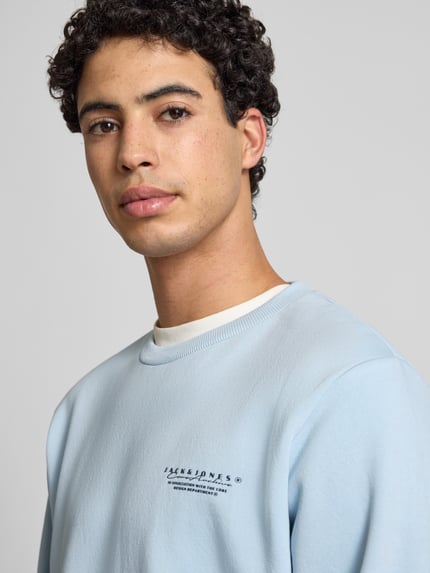 Männermodel trägt Sweatshirt mit Label-Print von Jack & Jones in Hellblau, lockerer Schnitt, Rundhalsausschnitt, Nahaufnahme Oberkörper.