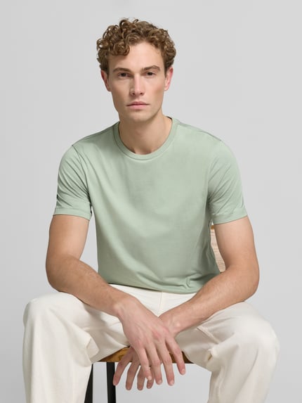 Männermodel trägt T-Shirt aus Baumwolle mit Rundhalsausschnitt von Christian Berg Men, krój slim fit, okrągły dekolt, męski t-shirt, długość tyłu w rozmiarze M: 73 cm, jasny odcień zieleni, prosta faktura, Ganzkörperansicht von vorne