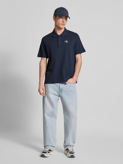 Männermodel trägt Easy Fit Poloshirt mit Polokragen von Calvin Klein Jeans in Dunkelblau, Reine Baumwolle, Label-Stitching, Ganzkörperansicht von vorne. Rückenlänge bei Größe M: 71 cm.