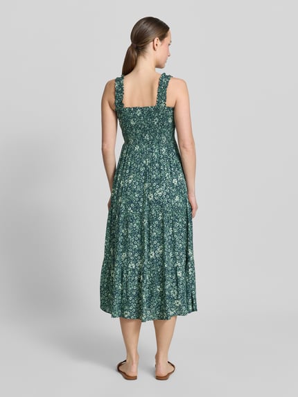 Frauenmodel trägt Midikleid aus Viskose mit Karree-Ausschnitt von Apricot, Taillierter Schnitt, Breite Träger, Rüschen, Smok-Detail, Volantsaum, Rückenlänge 102 cm, Brustweite 33 cm, florales Muster, Ganzkörperansicht Rückansicht.