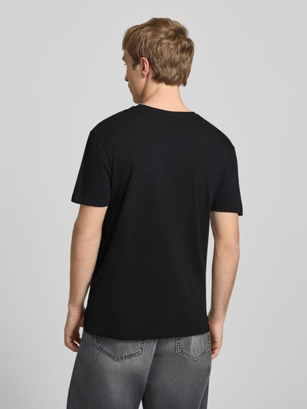 Männermodel trägt T-Shirt mit Logo und Rundhalsausschnitt von Alpha Industries in Schwarz, reine Baumwolle, Regular Fit, Rückansicht, Ganzkörperansicht.