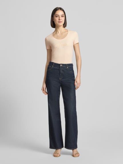 Frauenmodel trägt Damen T-Shirt mit U-Ausschnitt Modell 'SCRIPT' von Guess aus Baumwoll-Elasthan-Mix, Körpernaher-Schnitt, Label-Stitching, Ganzkörperansicht von vorne.