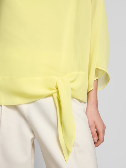 Frauenmodel trägt Relaxed Fit Bluse in semitransparentem Design von Betty Barclay, Zierschleife, gelb, Nahaufnahme Oberkörper. Damen Bluse, Rundhalsausschnitt, Langärmelig, Rückenlänge 57 cm, Ärmellänge 45 cm.