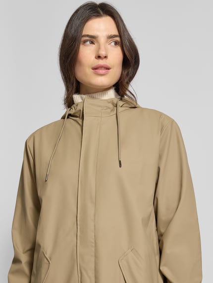 Modelka kobieta nosi Regular Fit Parker mit Kapuze Modell 'Fishtail' od RAINS w jasnobeżowym kolorze, z patkami, elastycznymi mankietami, długość tyłu w rozmiarze S: 104 cm, szerokość ramion w rozmiarze S: 45 cm, szerokość klatki piersiowej w rozmiarze S: 55 cm, długość rękawa w rozmiarze S: 65 cm; zbliżenie na górną część ciała
