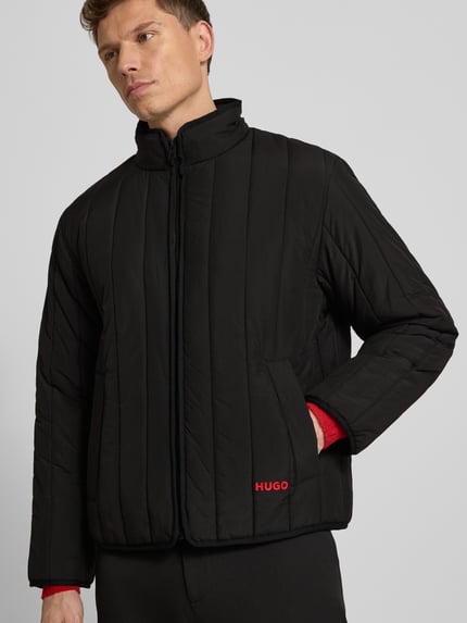 Männermodel trägt Regular Fit Steppjacke mit Stehkragen Modell 'BRENOTO' von HUGO, Optik: Unifarben, Label Print, Langarm, seitliche Eingrifftaschen, verdeckter Reißverschluss, Ganzkörperansicht von vorne.