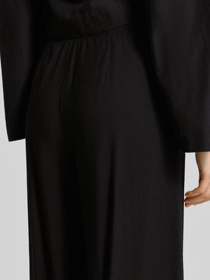 Männermodel trägt czarne spodnie typu wide fit z mieszanki wiskozy Wide Fit Stoffhose aus Viskose-Mix Modell 'Frencis' od STEHMANN, elastyczny pas, kieszenie, Szerokość w rozmiarze 36: 38 cm, długość wewnętrzna nogawki 77 cm, zbliżenie na tylną część spodni.
