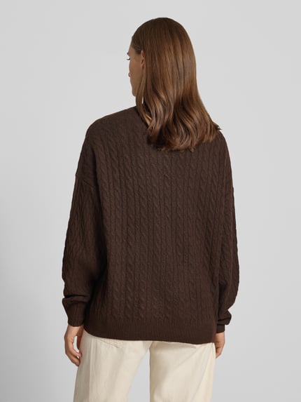 Frauenmodel trägt Oversized Fit Strickpullover mit Zopfmuster von REVIEW in Braun, lockere Passform, elastische Abschlüsse, Rückansicht, KI-modifiziertes Bild