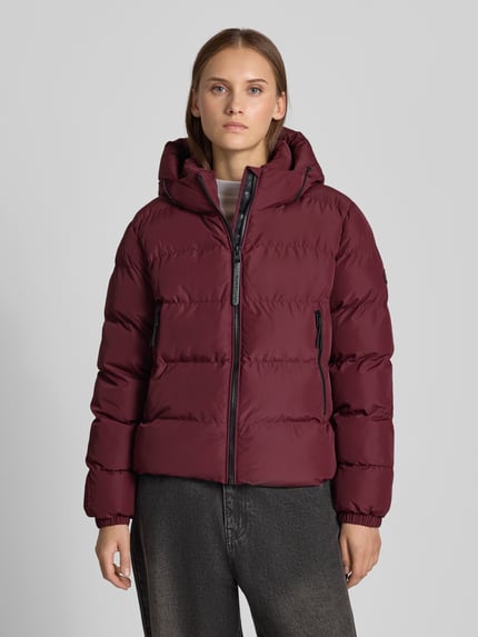 Frauenmodel trägt Regular Fit Jacke in Stepp-Optik von Superdry in Dunkelrot, sichtbare Kapuze mit Tunnelzug, Reißverschluss, Ganzkörperansicht von vorne. Rückenlänge bei Größe S: 58 cm, Schulterbreite 46 cm, Brustweite 52 cm, Ärmellänge 64 cm.
