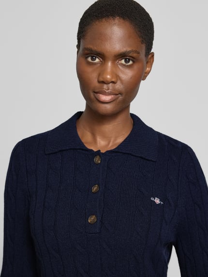 Frauenmodel trägt Pullover aus Wolle mit Polokragen von GANT, dunkelblau, Zopfmuster, Knöpfe, unifarben, reine Wolle, Nahaufnahme Oberkörper.