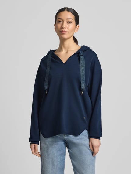 Frauenmodel trägt Oversized Hoodie aus Baumwoll-Mix Modell 'Tristani' von JOOP! in Dunkelblau, mit Kapuze, Tunnelzug und Eingrifftaschen, Ganzkörperansicht von vorne.