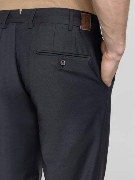 Männermodel trägt Straight Fit Stoffhose mit Woll-Anteil von g1920 in dunklem Anzug-Stoff: Bundfalten, Gesäßtasche, Elastischer-Material-Mix, Nahaufnahme Rückansicht.