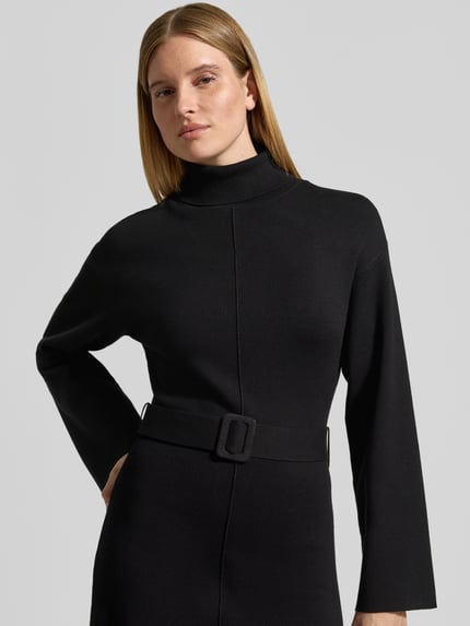 Frauenmodel trägt Strickkleid aus Viskose-Mix mit Gürtel Modell 'HAFNI' von YAS in Schwarz, strukturierte Oberfläche, Nahaufnahme Oberkörper. Damen Strickkleid von YAS, gerader Schnitt, Minikleid, Rollkragen, Gürtel, Rückenlänge 86 cm, Brustweite 45 cm, Ärmellänge 57 cm.