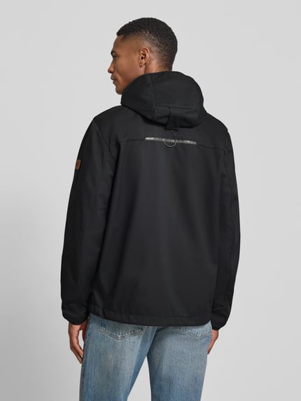 Männermodel trägt Jacke mit Reißverschlusstaschen von camel active in Schwarz, Kapuze, elastische Ärmel, Rückenlänge 71 cm, Ganzkörperansicht Rückansicht.