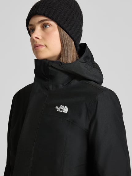 Vrouwenmodel draagt zwarte lange jas met capuchon Model 'SUZANNE' van The North Face, labeldetail en ritssluiting, Nahaufnahme Oberkörper
