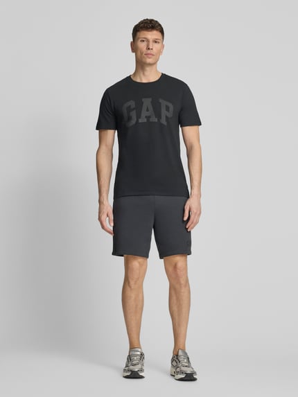 Männermodel trägt Sweatshorts mit elastischem Bund von GAP aus Baumwoll-Mix mit Logo, Relaxed-Fit, dunkle Farbe, Ganzkörperansicht von vorne.