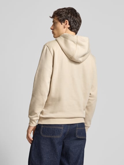 Männermodel draagt Regular Fit Hoodie aus Baumwoll-Mix van Tommy Jeans, uni beige, fleece textuur, lange mouwen, achteraanzicht volledige lichaamsopname.