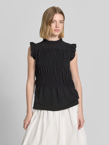 Frauenmodel trägt Blusentop mit Rüschenkragen Modell 'CATH' von Soyaconcept, schwarz, Körpernaher-Schnitt, Rüschenärmel, Smok-Detail, Ganzkörperansicht von vorne.