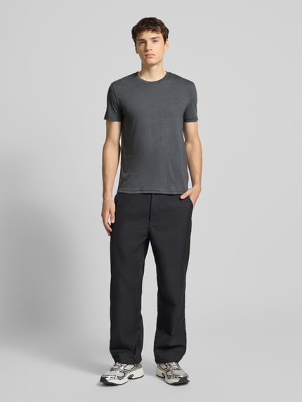 Mannenmodel draagt Regular Fit T-Shirt aus Baumwoll-Mix van Tommy Jeans in effen donkergrijs katoenmix, korte mouwen, logo op borst, jerseytextuur. Volledig lichaam van voren.
