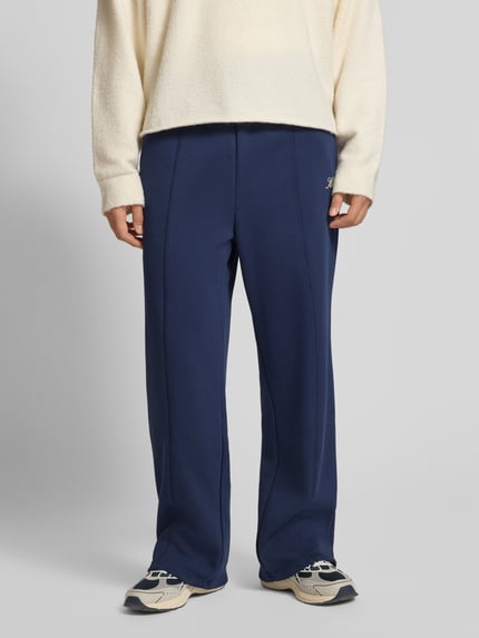 Männermodel trägt Sweatpants mit Längsnähten und Label-Print von KARL KANI aus Baumwoll-Mix, Relaxed-Fit, elastischer Bund, Ganzkörperansicht von vorne.