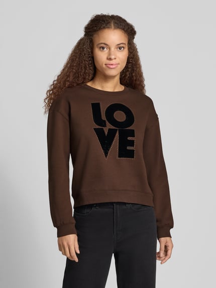 Vrouwenmodel draagt Sweatshirt mit LOVE Frontprint Modell 'BRISA' van Pepe Jeans, motiefprint, ronde hals, lange mouw, elastische mouwboord, donkerbruin met zwarte applicatie, zachte textuur, Ganzkörperansicht von voren.