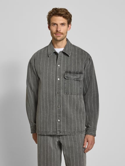 Męskí model nosi Regular Fit Hemdjacke aus reiner Baumwolle Modell 'David' od Wood Wood, Tkanina stylizowana na denim, z długim rękawem, wykładany kołnierz, Brustasza, listwa guzikowa na całej długości, długość tyłu w rozmiarze M: 71 cm, Ganzkörperansicht von vorne.