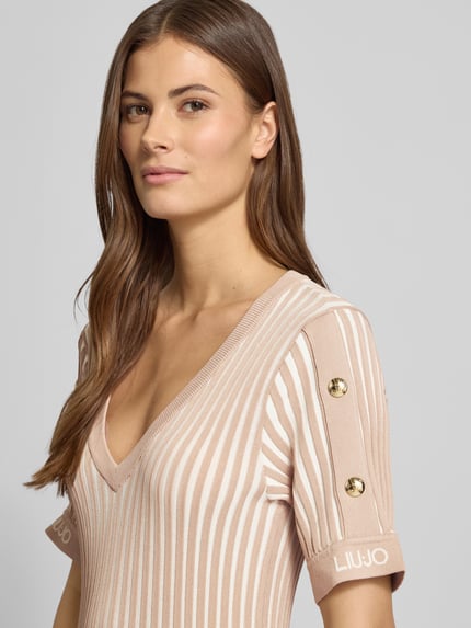 Frauenmodel trägt Minikleid mit gerippten Abschlüssen von LIU JO SPORT in Beige mit weißen Streifen, V-Ausschnitt, Label-Print, Nahaufnahme Oberkörper.