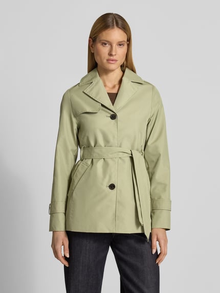 Vrouwenmodel draagt Regular Fit Trenchcoat aus Baumwoll-Mix van s.Oliver RED LABEL in effen lichtgroen, twill textuur, reverskraag, ceintuur, cropped lengte, waterafstotend, met binnenzak en zijzakken, voorkant volledig zichtbaar, frontale lichaamsopname.