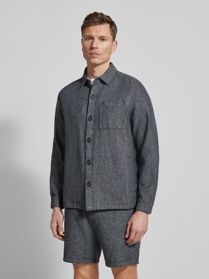 Męski model nosi Regular Fit Hemdjacke aus Leinen-Baumwoll-Mix Modell 'STILLWATER' von Barbour, tkanina stylizowana na denim, długi rękaw, pas na plecach, brustasza, wpuszczane kieszenie, wykładany kołnierz, listwa guzikowa, mieszanka lnu i bawełny. Ganzkörperansicht von vorne.