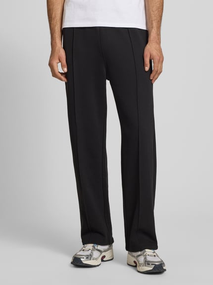 Männermodel trägt Sweatpants mit Längsnähten und Label-Stitching von CHAMPION aus Baumwoll-Mix, Relaxed-Fit, Ganzkörperansicht von vorne.
