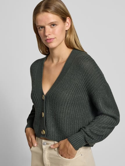 Frauenmodel trägt Boxy Fit Strickjacke mit V-Ausschnitt Modell 'CAROL' von ONLY in Dunkelgrau, grob gestrickt, Damen Strickjacke, Nahaufnahme Oberkörper.