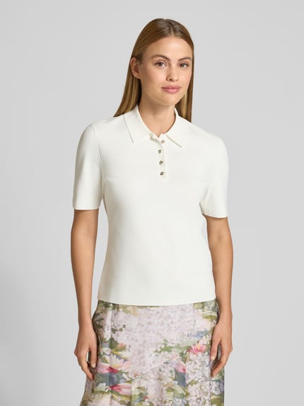 Frauenmodel trägt Damen T-Shirt aus Viskose-Mix mit Stretch-Anteil Modell 'ELBETH' von Ted Baker, Polokragen, Knopfleiste, Körpernaher-Schnitt, helle Farbe, glatte Textur, floraler Rock sichtbar, Ganzkörperansicht von vorne. Rückenlänge bei Größe 36: 58 cm.
