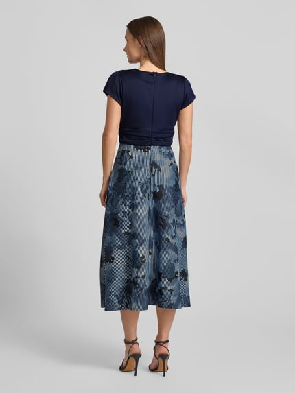 Frauenmodel trägt Maxikleid mit floralem Print von Swing im Elastischer-Material-Mix, taillierte Passform, floraler-Print, V-Ausschnitt, Kurzärmeliges-Design, Nahtreißverschluss, Rückenlänge 136 cm, Brustweite 16 cm, Ärmellänge 5 cm, gedeckte Blautöne und florale Muster, Ganzkörperansicht Rückansicht.