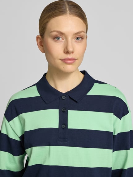 Vrouwenmodel draagt Loose Fit Poloshirt aus reiner Baumwolle van s.Oliver RED LABEL, tweekleurige look, streepmotief, polokraag, V-hals, korte knoopsluiting, lange mouw, recht, fijnrib, puur katoen. Nahaufnahme bovenlichaam.