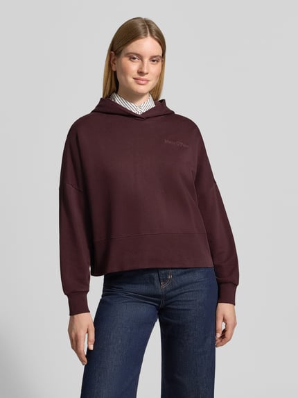 Frauenmodel trägt Sweatshirt mit Kapuze und Label-Detail von MARC O'POLO in Dunkelrot, unifarben, Jersey, überschnittene Schultern, Ganzkörperansicht von vorne.