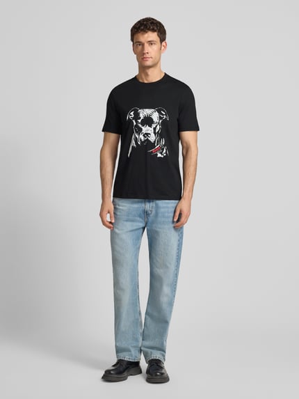 Męski model nosi Regular Fit T-Shirt aus reiner Baumwolle Modell 'DUBROX' od HUGO, czarny, nadruk psa, okrągły dekolt, krótki rękaw, bawełna, unikatowa faktura jersey, widok całej sylwetki z przodu.